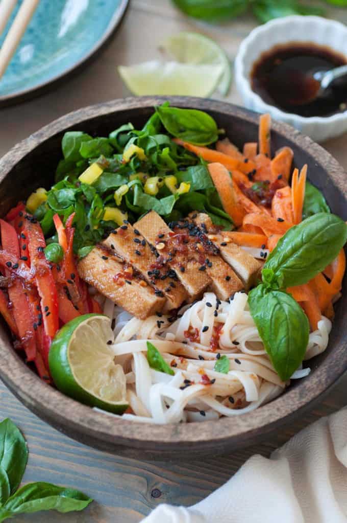 Chilled Smoked Tofu Sesame Rice Noodle Salad in a wooden bowl with soy sauce and lime wedges in the background