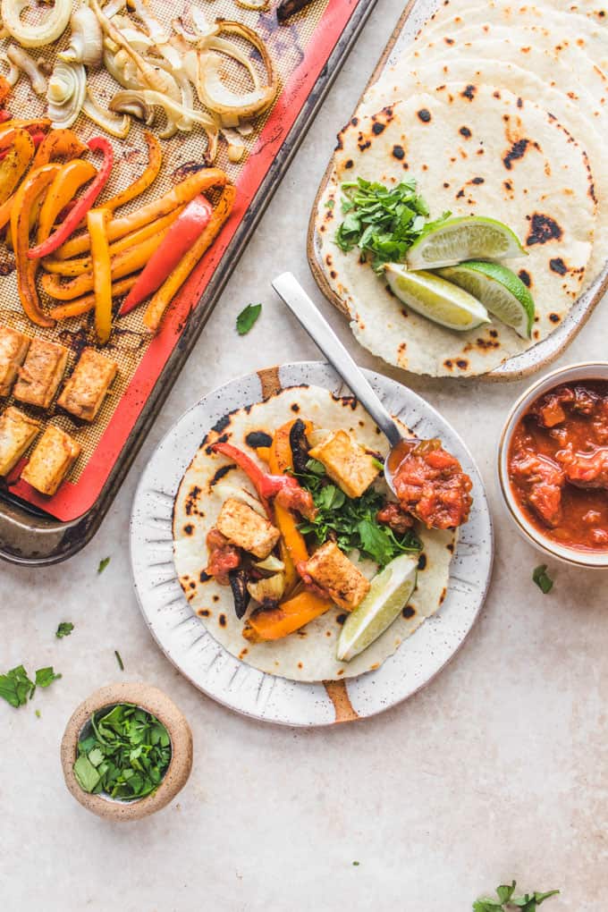 a sheet pan with fajitas and chipotle tofu with two plates on the side with tortillas and lime