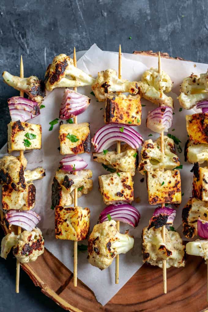 Five Afghan Cauliflower and Tofu Tikka Kebab Skewers on a Wooden Board on a black counter top