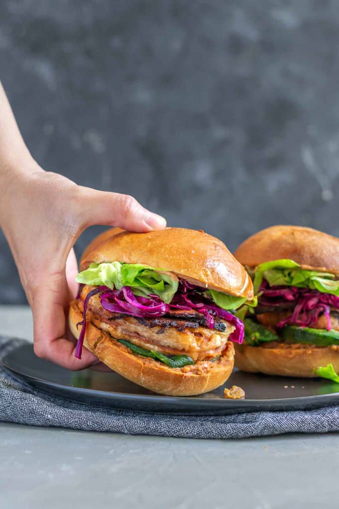 a hand holding a tofu burger with another burger in the background