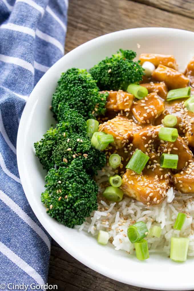 Sweet and Salty Tofu with Broccoli over Rice in a White Bowl with a Blue Napkin on the Side