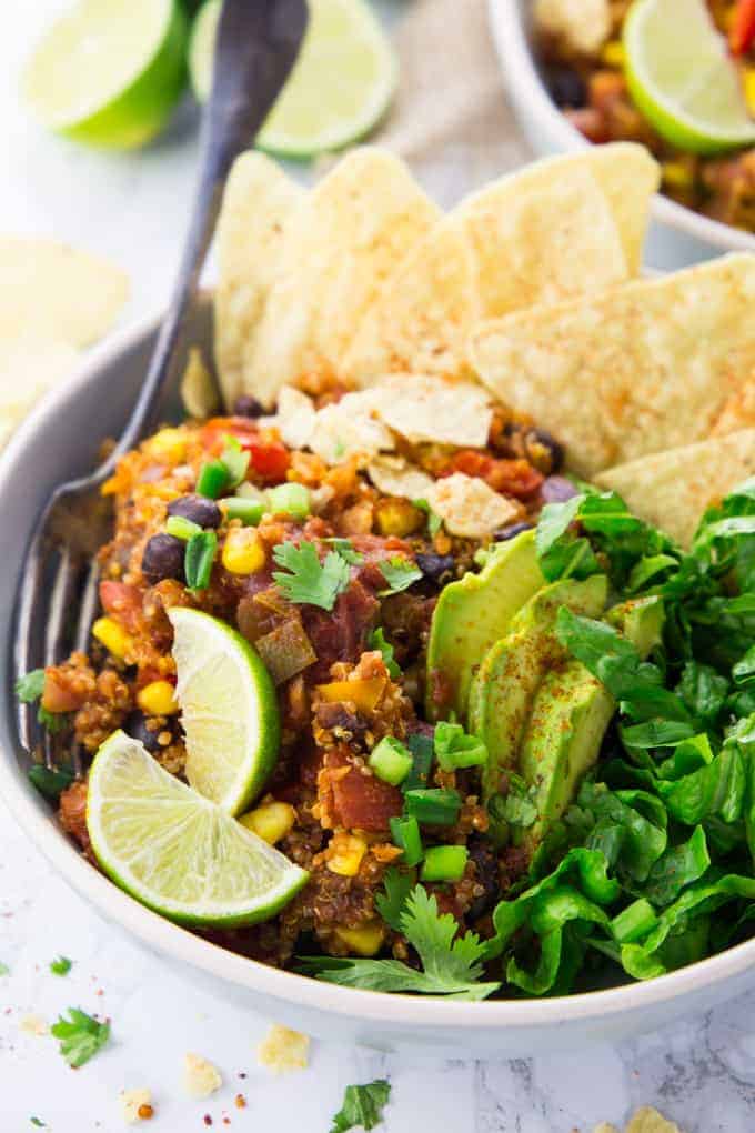 vegan chili with quinoa in a grey bowl with lettuce and tortilla chips on the side and limes in the background