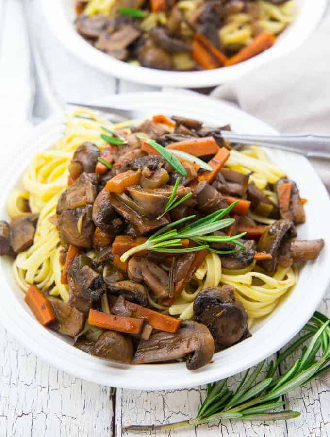 mushroom bourguignon with fettuccine on a white plate with fresh rosemary on top and on the side 