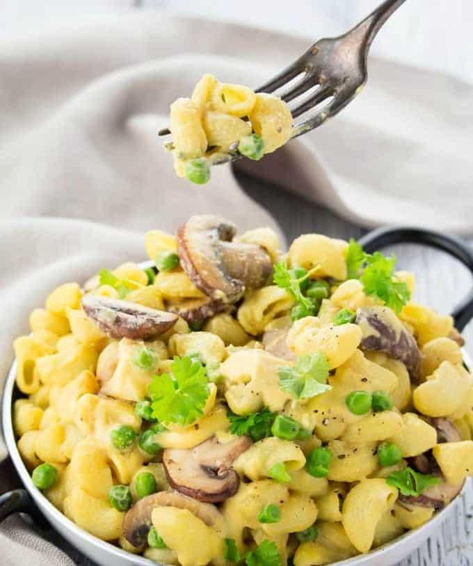 A fork picking up some vegan mac and cheese with peas and mushrooms in a pan