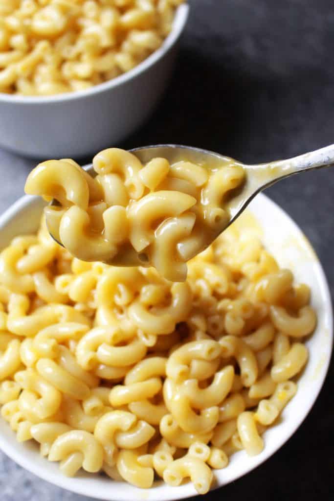 A spoon with vegan mac and cheese over a bowl with pasta