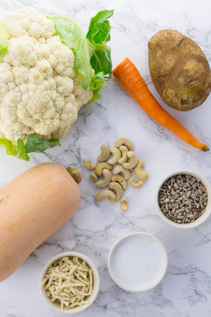 Ingredients you can use as a base for vegan mac and cheese on a marble counter top (cauliflower, carrot, potato, butternut squash, cashews, coconut milk, vegan cheese, and sunflower seeds)