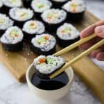 vegan sushi on a wooden board with one piece of sushi being dipped into a small bowl of soy sauce in the front