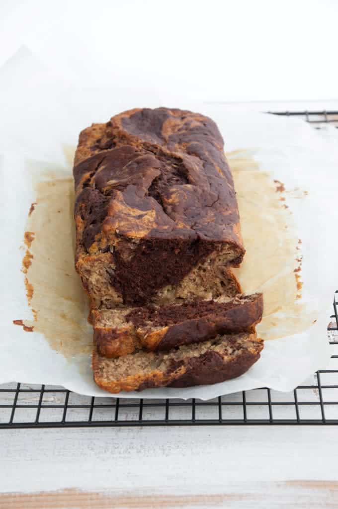 marbled banana bread on a cooling rack on a white wooden su