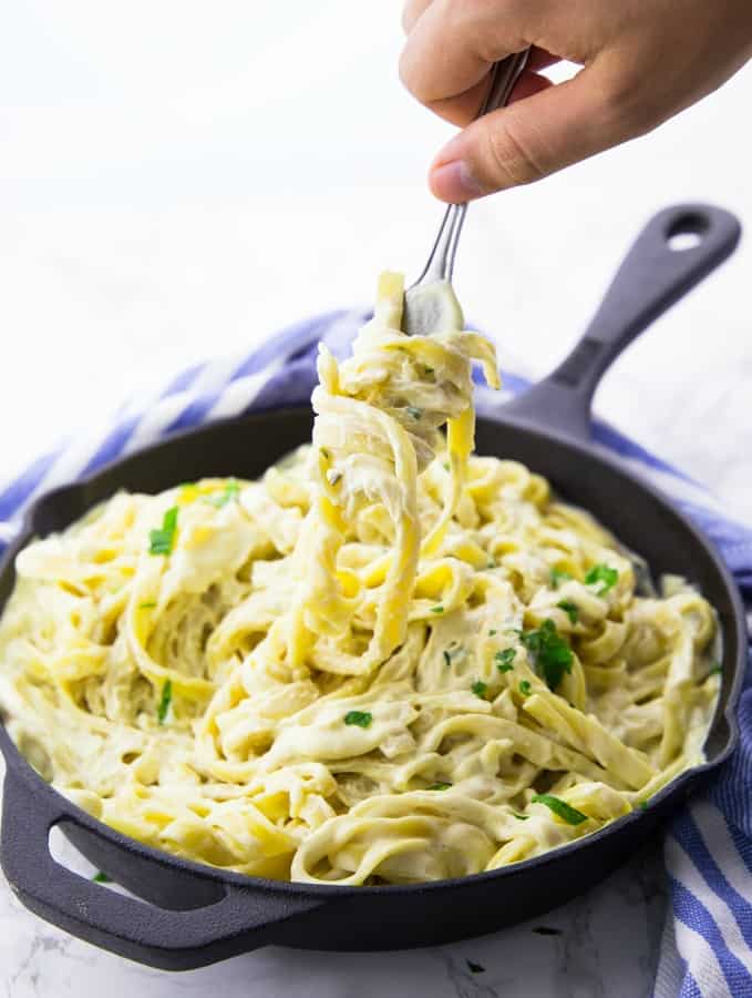 a hand picking up fettuccine with a fork in a black pan