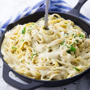 fettuccine with vegan cauliflower Alfredo sauce in a black pan with a fork and a blue dish cloth in the background