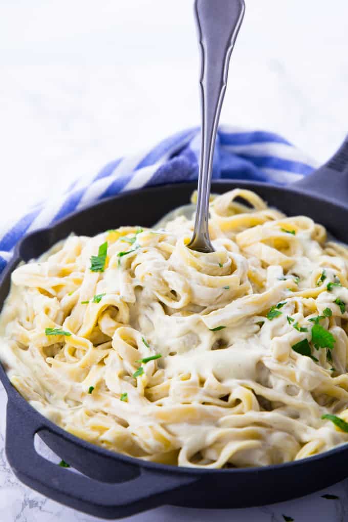 fettuccine with vegan cauliflower Alfredo sauce in a black pan with a fork and a blue napkin in the background