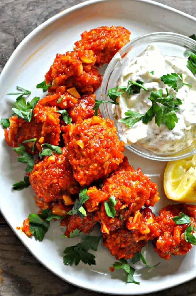 buffalo sprouts on a white plate with a small bowl of garlic sauce and a slice of lemon on the side and parsley on top 