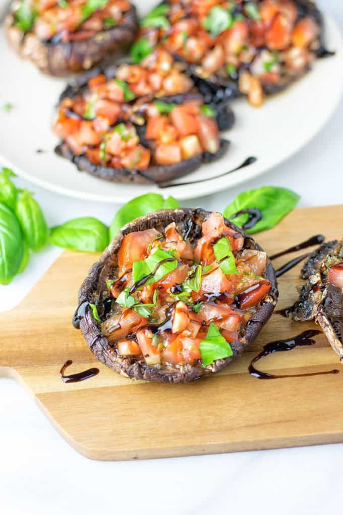 Portobello Mushroom Bruschetta on a wooden board with basil on the side and balsamic reduction on top 