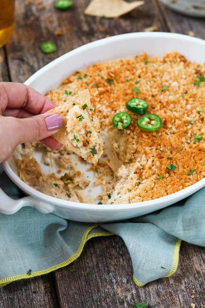 Vegan Jalapeno Popper Dip in a white bowl and a hand dipping a nacho into the dip 