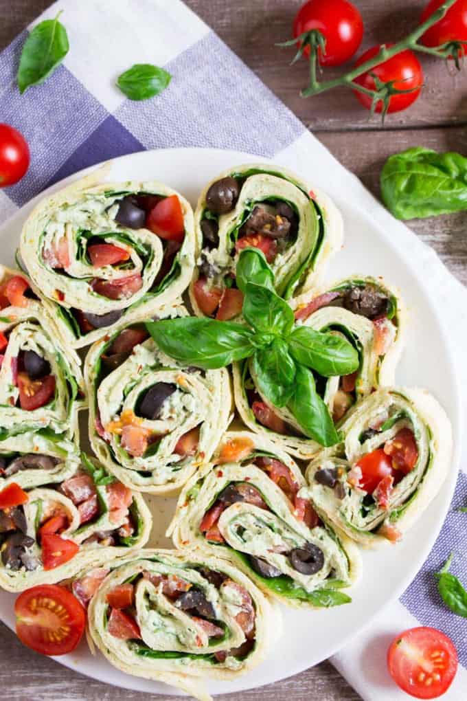 vegan pinwheels filled with spinach ricotta, olives, and cherry tomatoes on a white plate with a blue dish cloth and cherry tomatoes on the side
