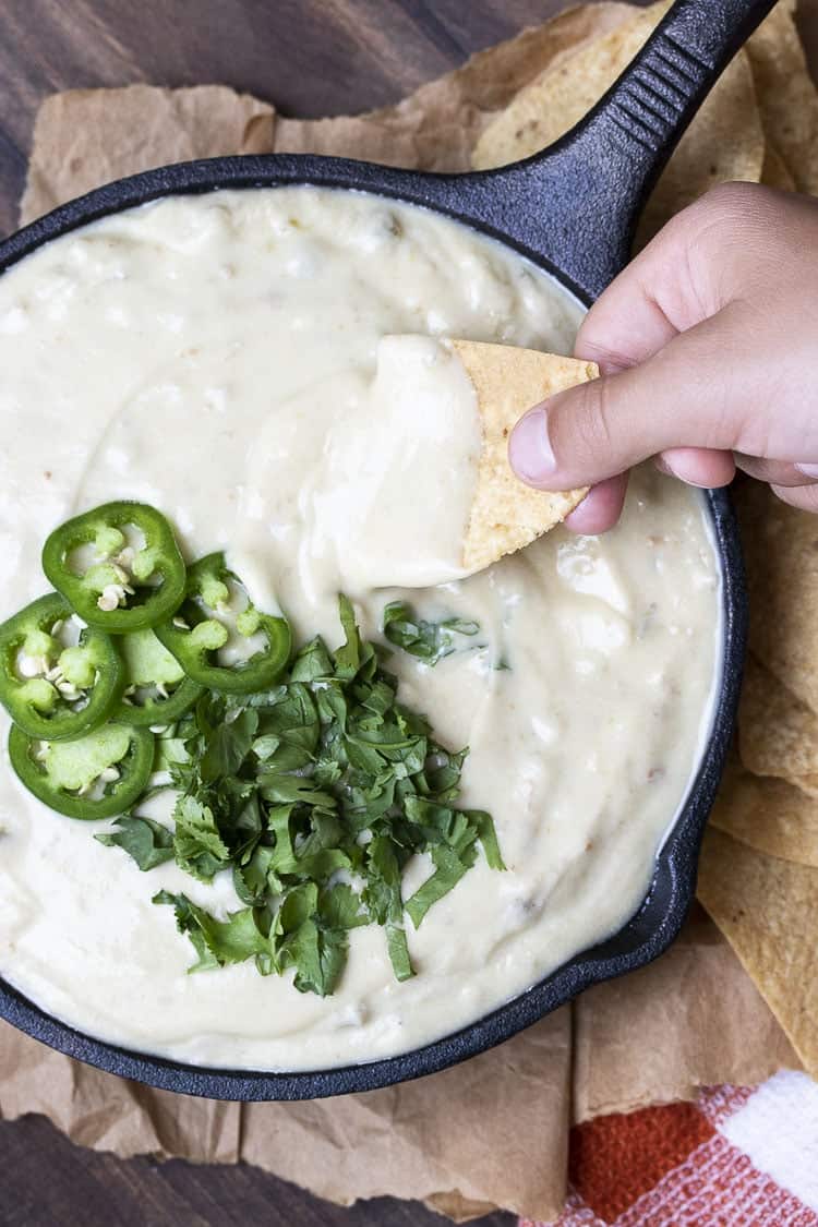 vegan queso dip in a black cast iron skillet with a hand dipping a nacho in the dip