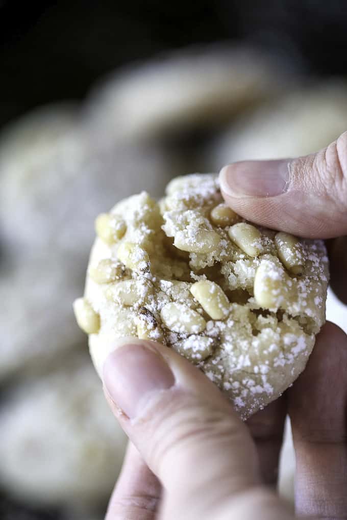 a hand holding a pignoli Cookie with more cookies in the background