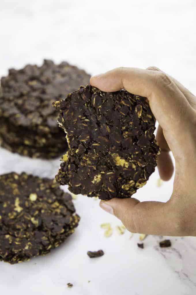 a hand holding a no bake cookie over a marble counter top with more cookies in the background