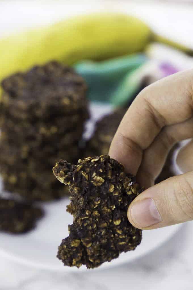 a hand holding a chocolate banana cookie with more cookies and a banana in the background