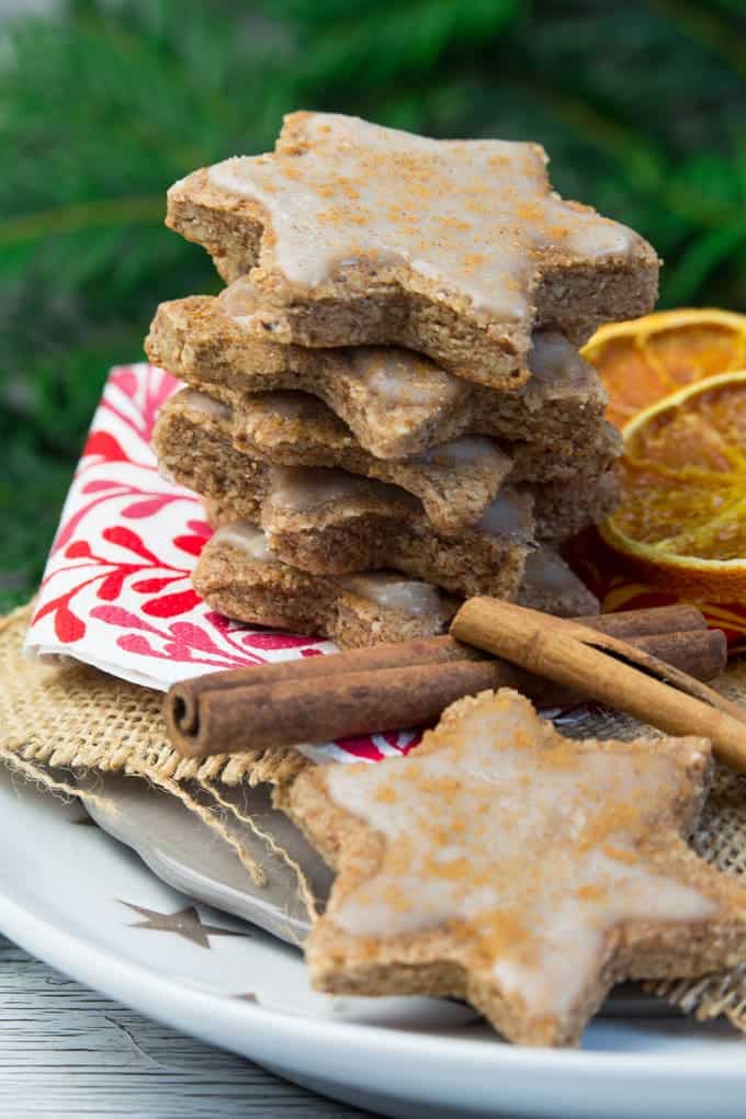 a stack of star-shaped vegan cinnamon orange cookies on a white plate with dried orange slices and cinnamon sticks on the side