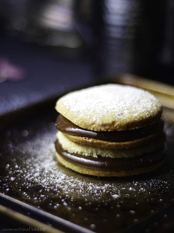 a stack of Alfajores cookies on a black plate with powdered sugar on top