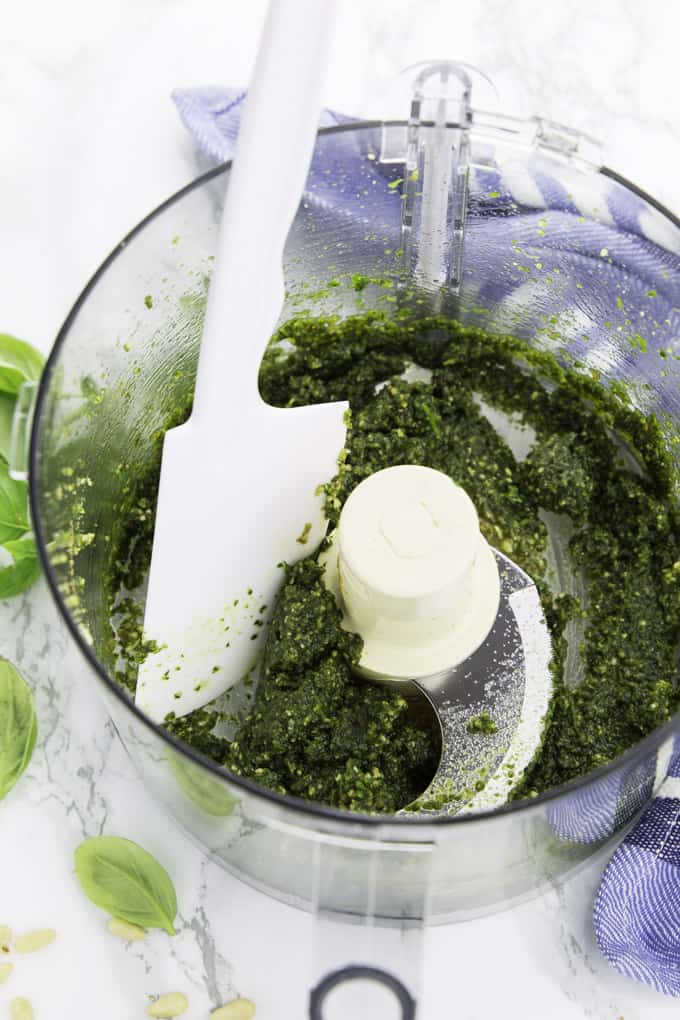pesto in a food processor with a spatula on a marble counter top 