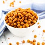 a hand eating roasted chickpeas out of a small white bowl on a marble counter top