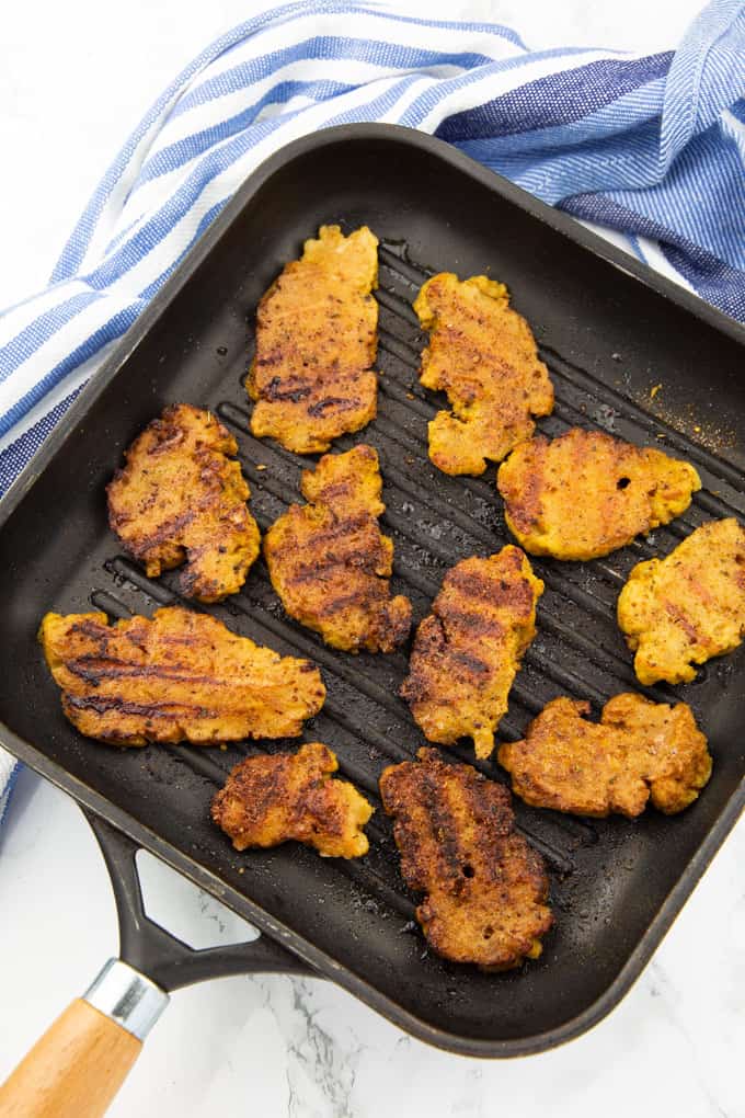 seasoned seitan slices in a grill pan on a marble counter top with a blue dish cloth on the side 