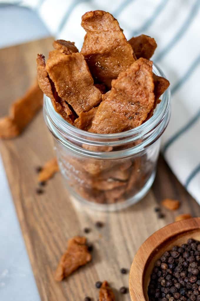 seitan jerky in a glas on a wooden board with more jerky on the side 