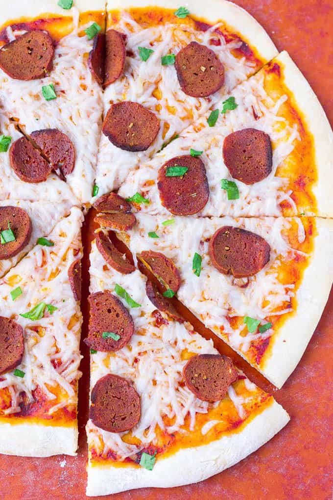 a sliced vegan pizza with seitan pepperoni on a red surface 