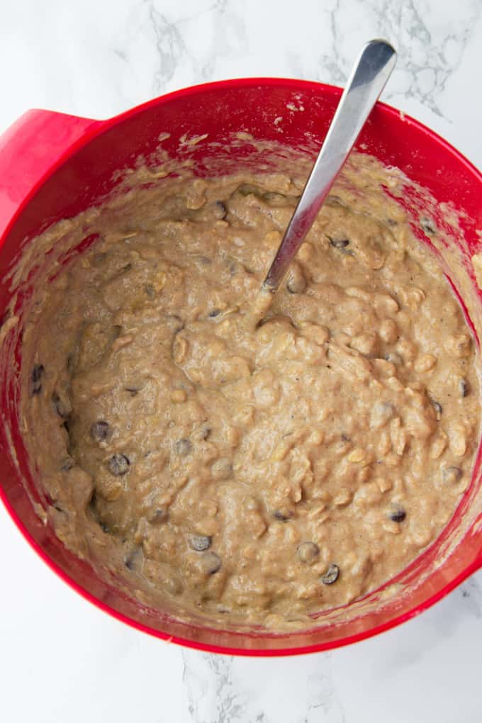 batter for vegan banana muffins in a red bowl with a spoon on a marble counter top 