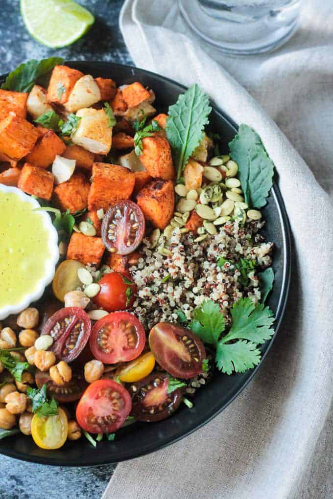 a sweet potato quinoa bowl in a black bowl with a lime wedge and a glass of water on the side 