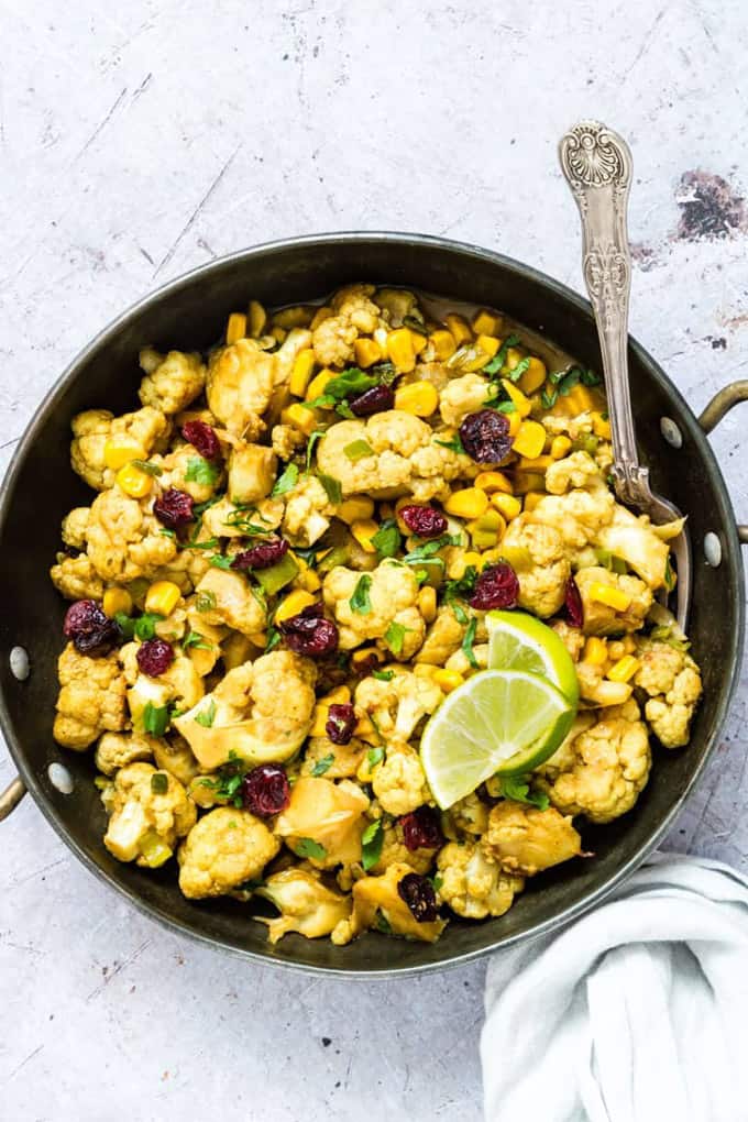 One Pan Cauliflower Curry on a concrete counter top with a spoon and two lime wedges on top