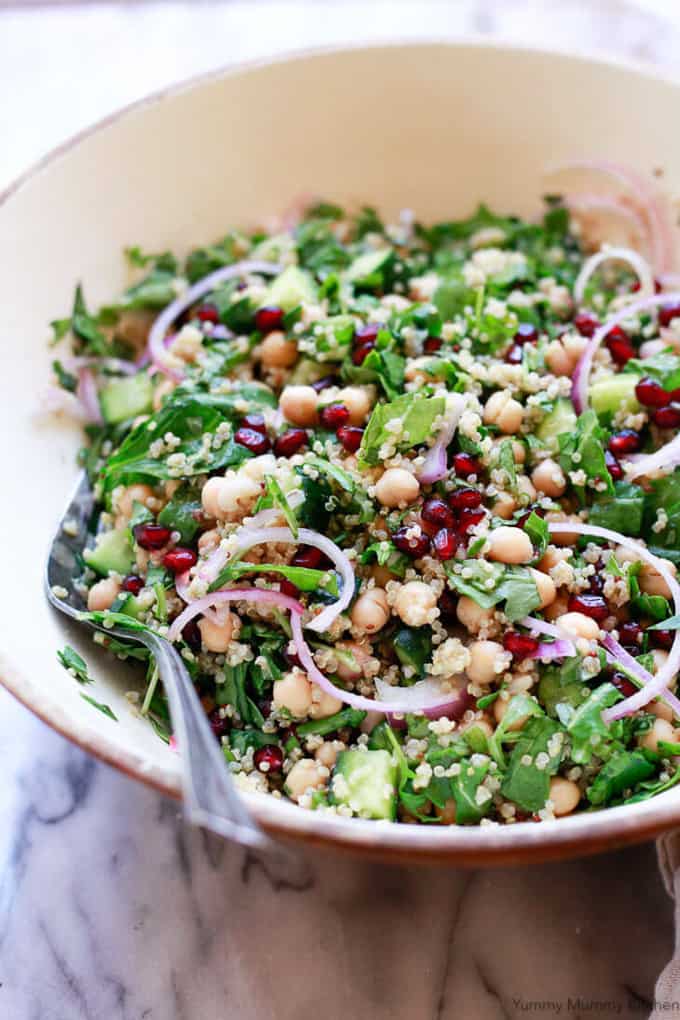 chickpea quinoa salad with spinach in a white bowl with a spoon on a wooden counter top 