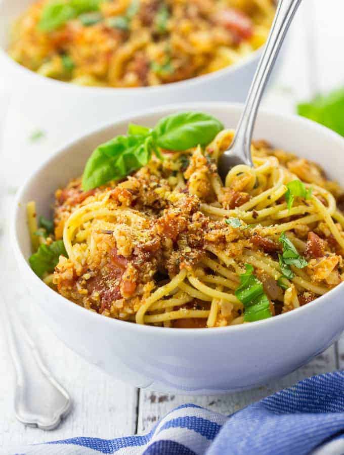 spaghetti with cauliflower bolognese in a white bowl on a white wooden counter top with another bowl in the background 