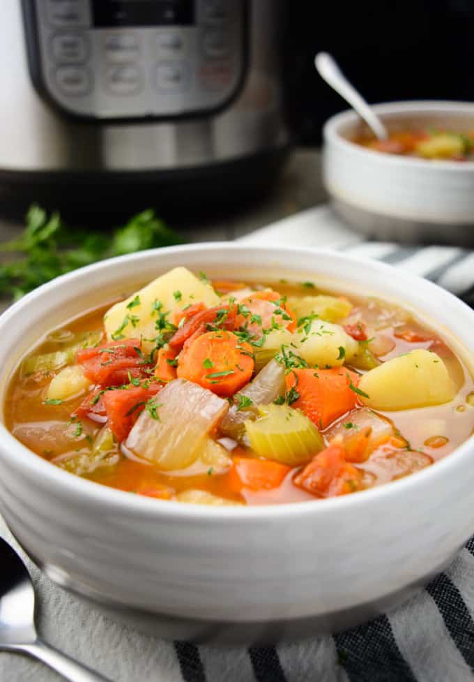Instant Pot vegetable soup in a a white bowl with an Instant Pot and another bowl of soup in the background 