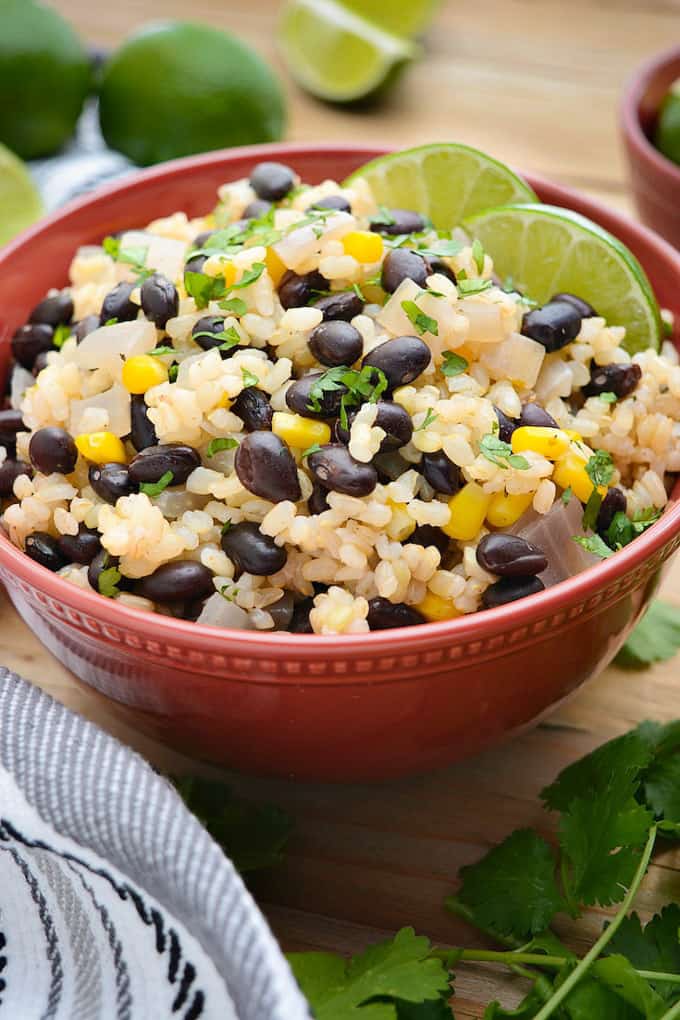 rice with black beans and lime in an orange bowl on a wooden counter top with lime wedges and cilantro on the side 