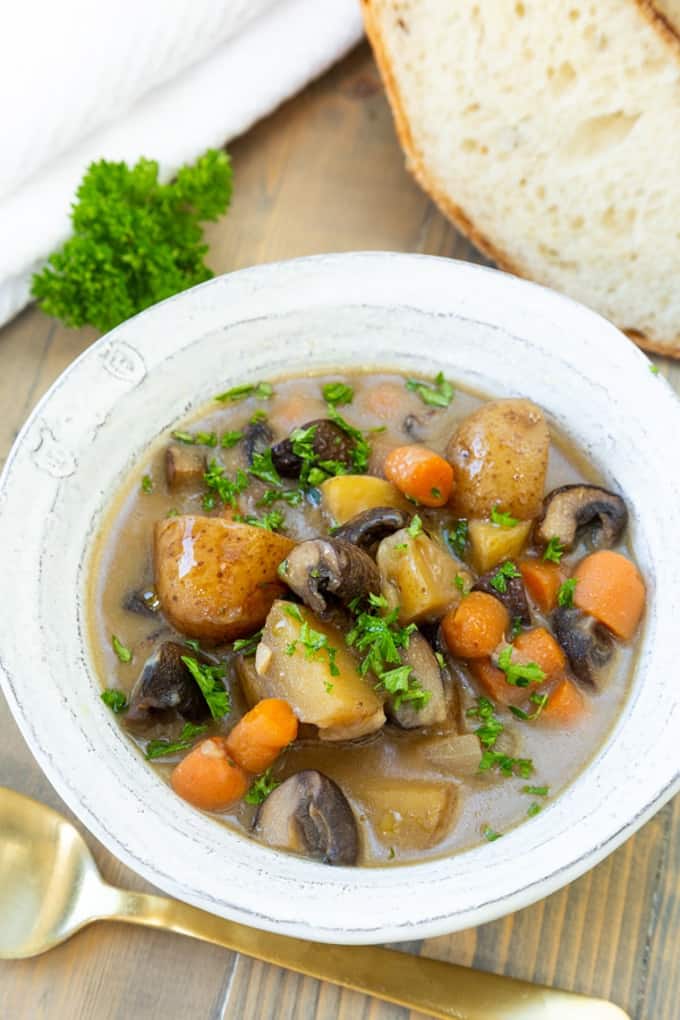 vegan beef stew in a white bowl with a slice of bread and a spoon on the side 