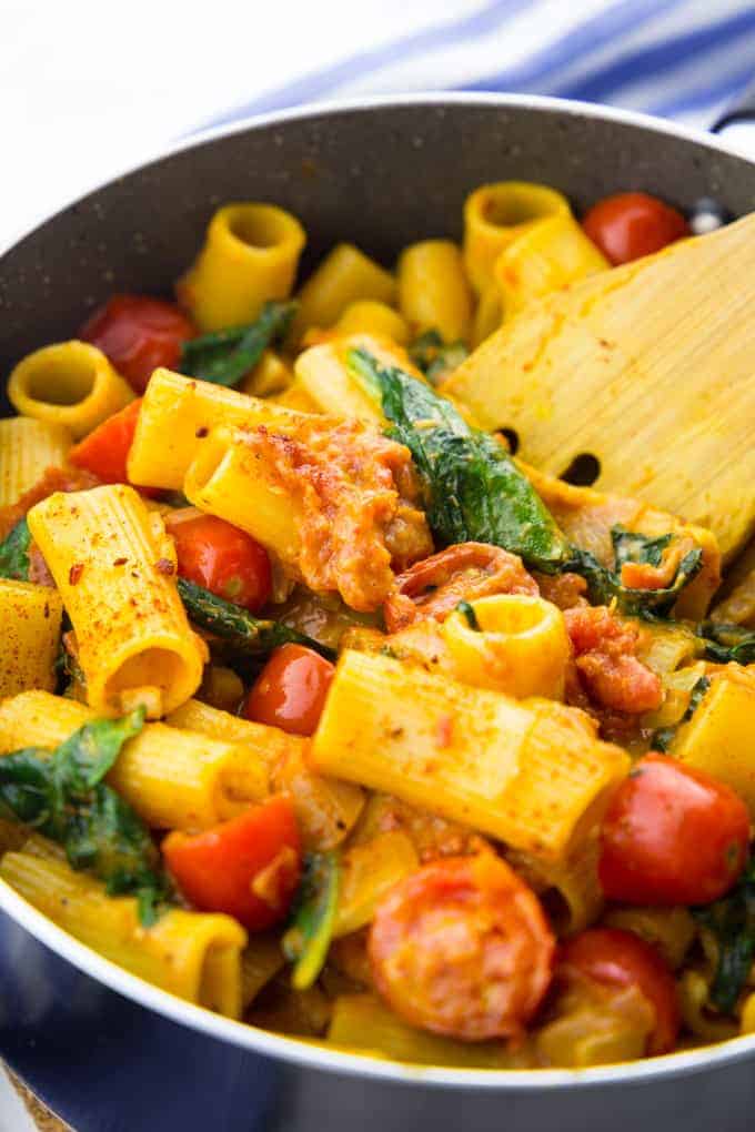 vegan one pot pasta with spinach and tomatoes in a black pot with a wooden spoon 