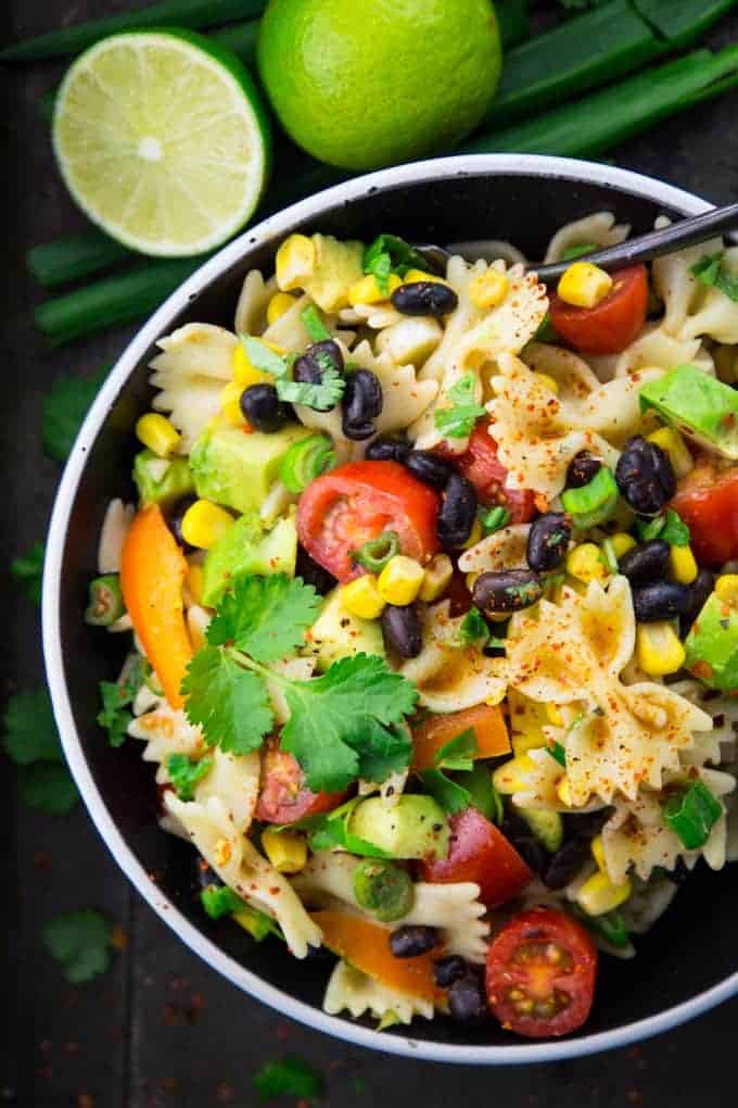 southwestern pasta salad in a black bowl with a spoon and two limes and green onions in the background 