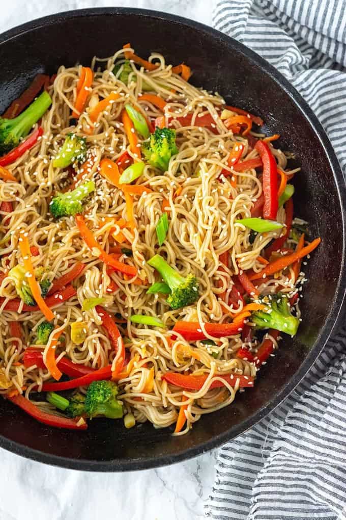 Vegetable Lo Mein in a black pan on a marble counter top with a dish cloth on the side 