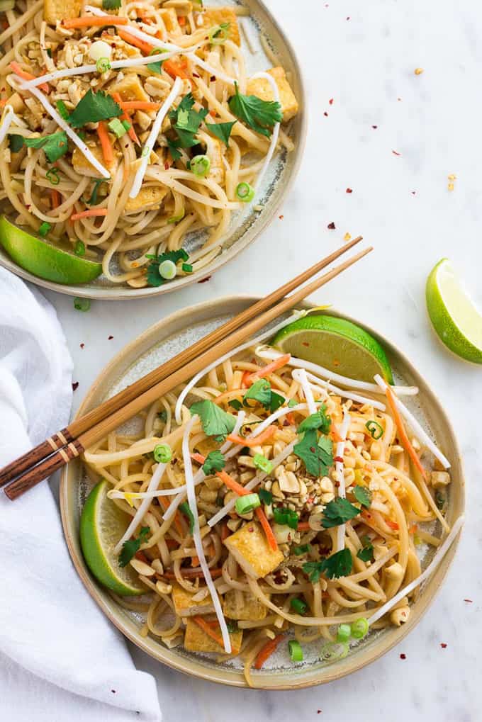 two plates of vegan pad Thai with chop sticks on a white counter top with a lime wedge on the side 