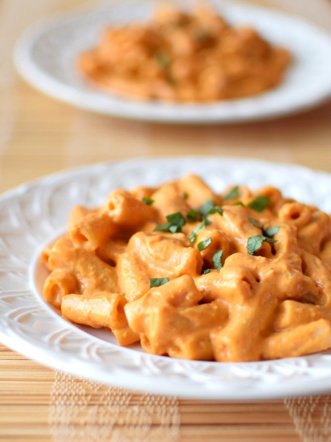 penne with creamy vegan vodka sauce on two white plates on a wooden counter top 