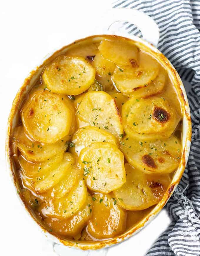 Vegan Potatoes Au Gratin in a white baking dish on a white counter top with a blue dish towel on the side 