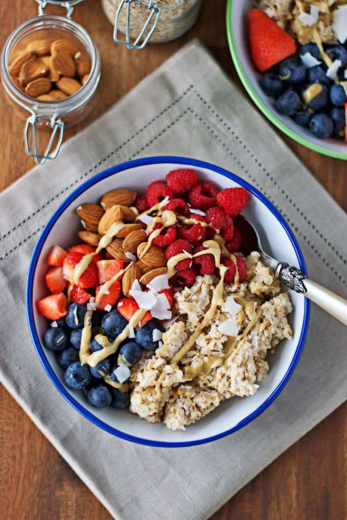 a breakfast bowl with quinoa, berries, and almonds on a wooden counter top on top of a grey dish cloth 