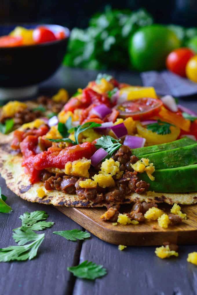 a Vegan Breakfast Taco on a wooden board with avocado slices, cherry tomatoes, red onion, and fresh cilantro on top and on the side 