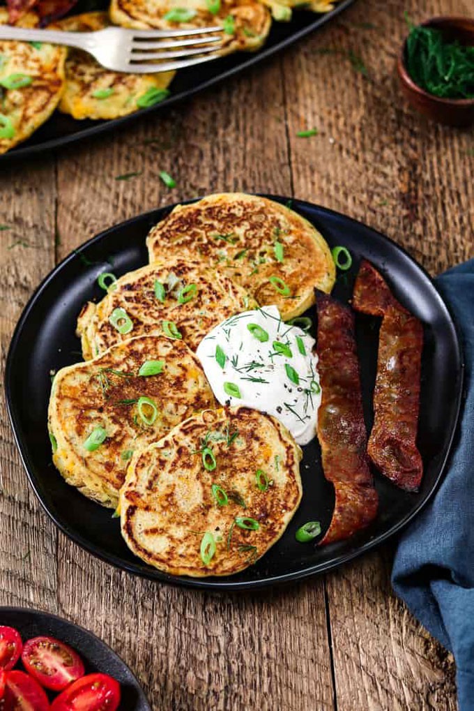 four savory vegan pancakes on a black plate with vegan bacon on the side on a wooden counter top 