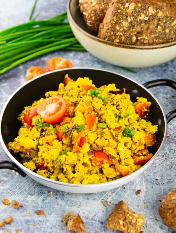 tofu scramble in a small pan on a blue counter top with a bowl of buns and fresh chives in the background