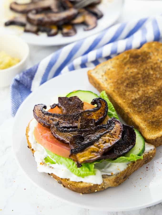vegan bacon made of mushrooms on a sandwich with tomatoes and lettuce on a white plate 