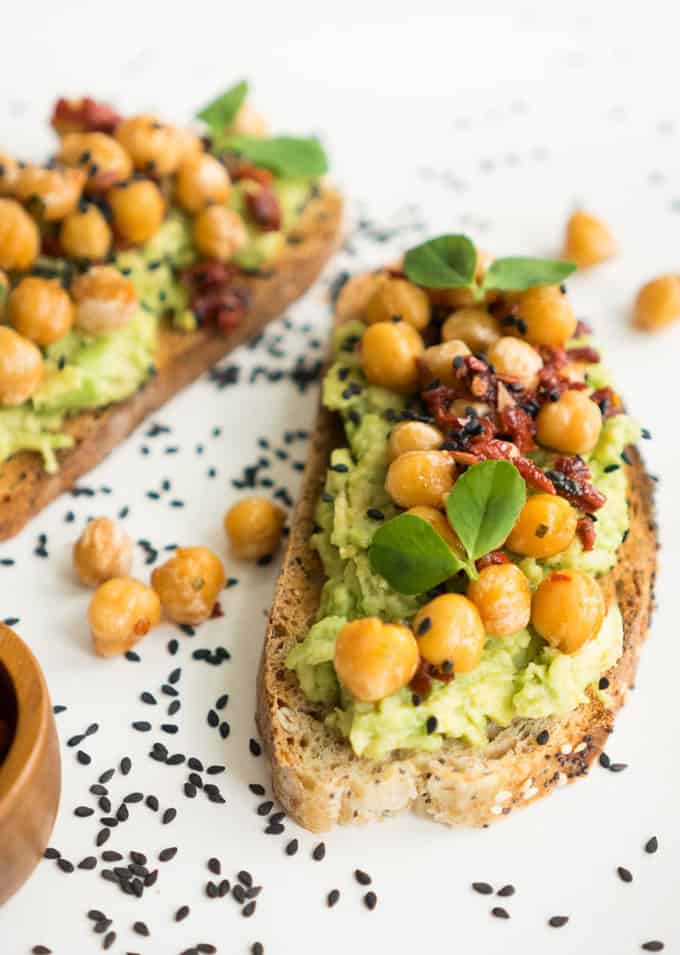 two slices of bread with mashed avocado and chickpeas on a white counter top 